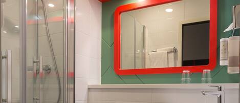 A modern bathroom with a glass shower enclosure, a white sink, and a red-framed mirror.