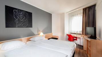 Ein Hotelzimmer mit einem großen Bett, einem Schreibtisch mit Stuhl, einem Fernseher und einem Bild an der Wand.