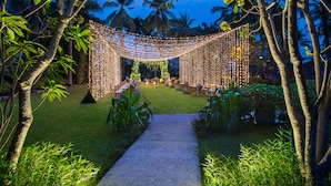 Un camino que lleva a un área exterior decorada con luces colgantes y plantas tropicales.