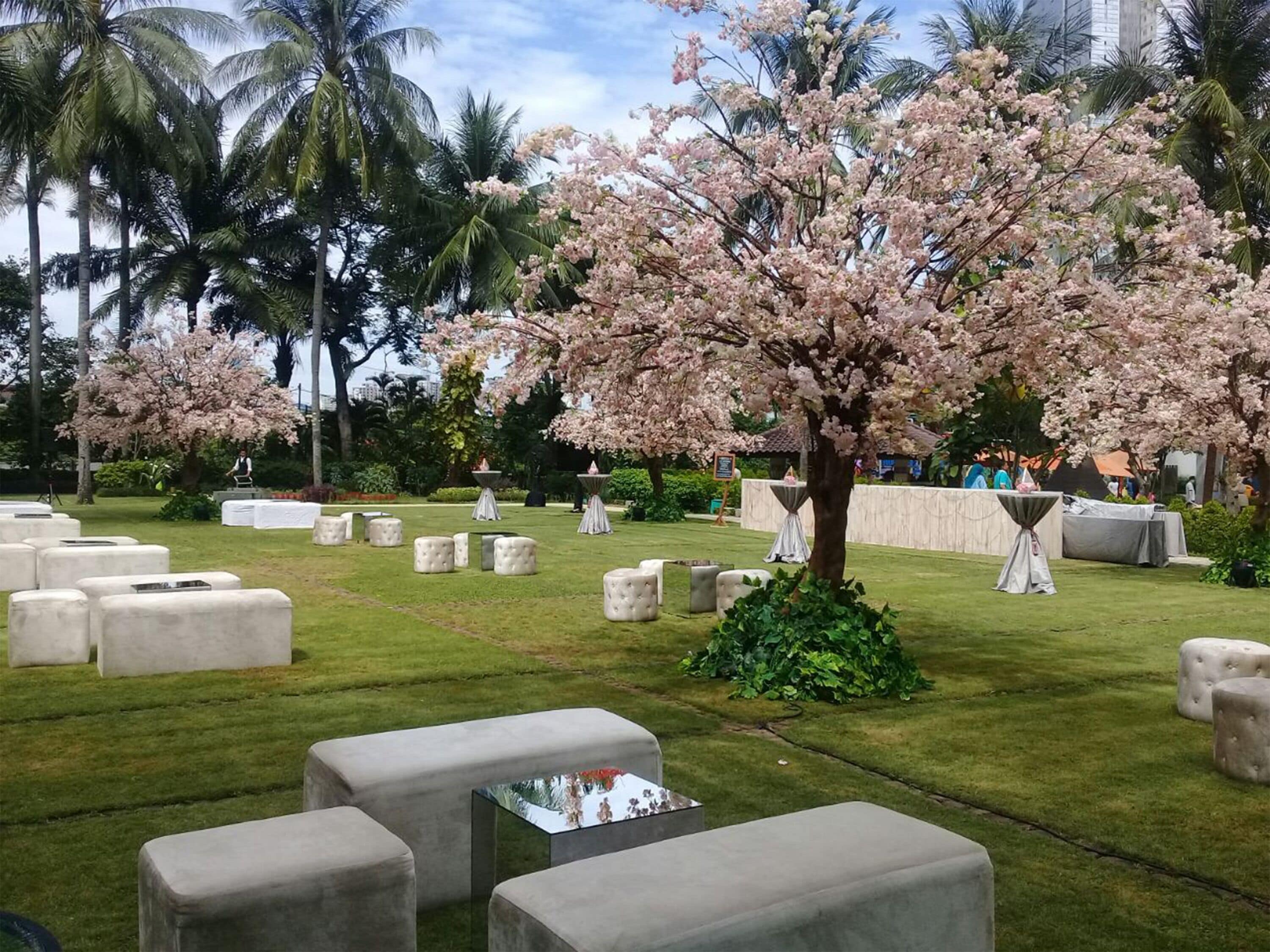 Ein Garten mit einem großen, blühenden Baum, mehreren Sitzbereichen und einem gepflegten Rasen.