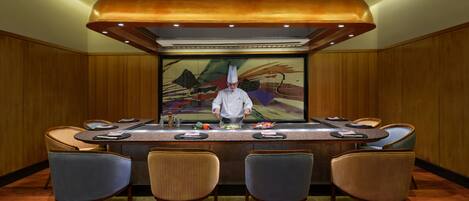 Un chef preparando comida en una barra con cuatro sillas al frente.