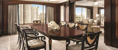 A spacious dining area with a long table and chairs, large windows with curtains, and a view of a cityscape.