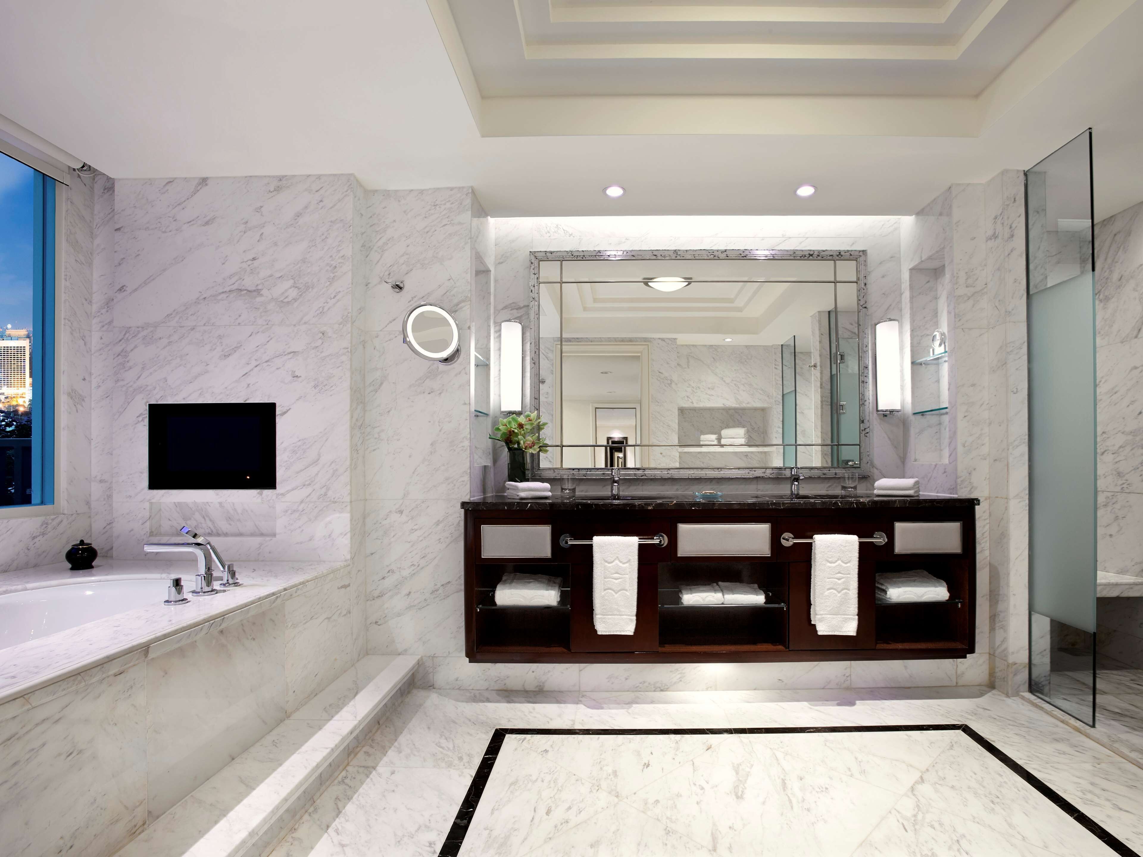 A modern bathroom with a marble floor, a large mirror, a dual sink vanity, and a glass shower enclosure.