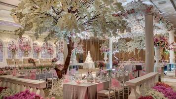 A grand hall with a large artificial tree, elegant tables, and abundant floral decorations.