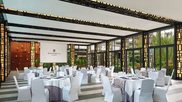 A banquet hall with round tables, white chairs, and a large screen displaying "SHANGRI-LA JAKARTA".