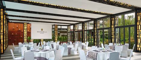 A banquet hall with round tables, white chairs, and a large screen displaying "SHANGRI-LA JAKARTA".