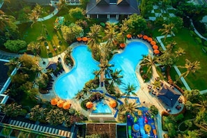 An aerial view of a resort with a large central swimming pool, surrounded by palm trees and outdoor seating areas. - Shangri-La Jakarta (Jakarta)