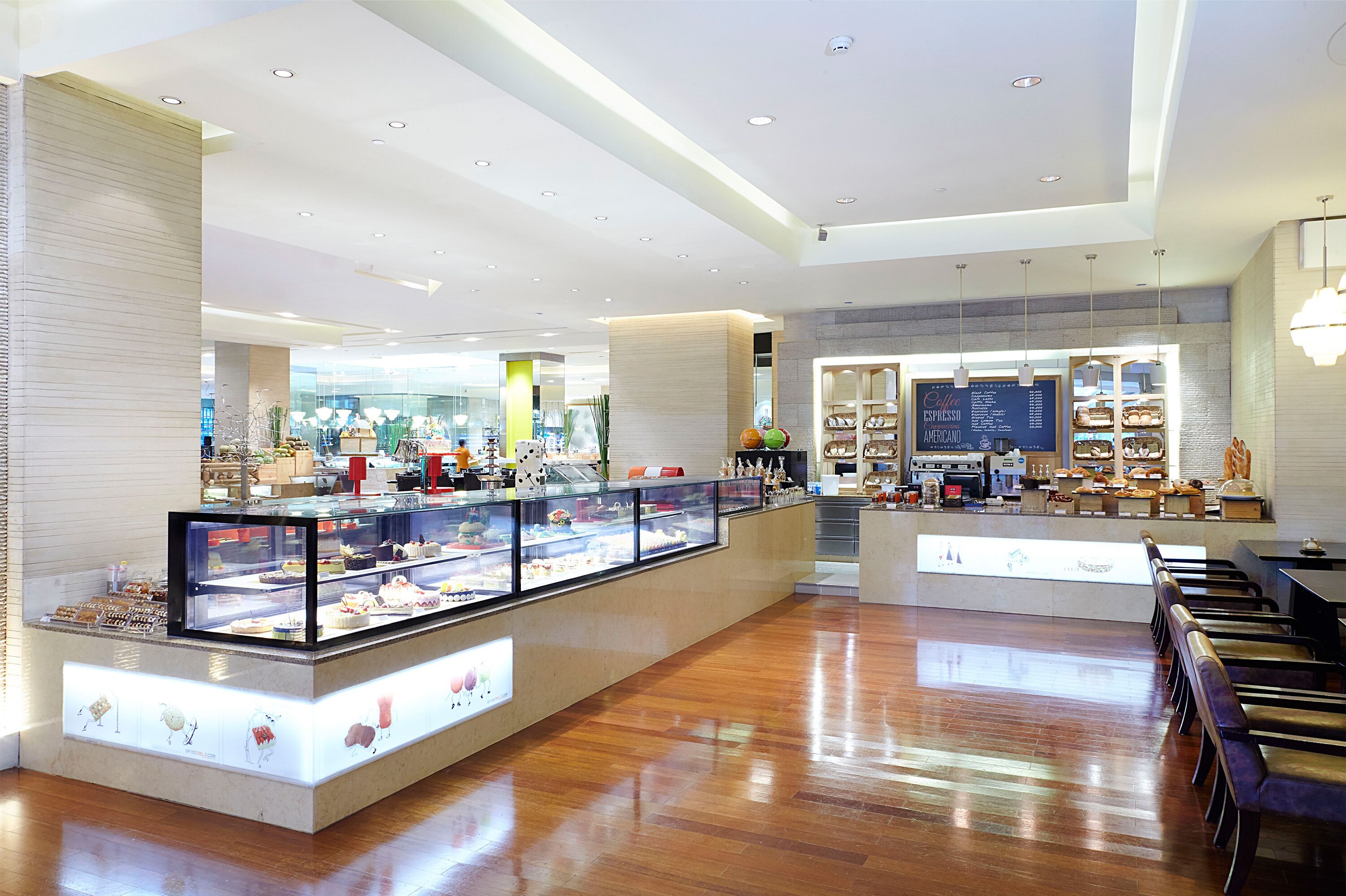 A modern cafe with a central display case of pastries, wooden flooring, and a seating area with tables and chairs.
