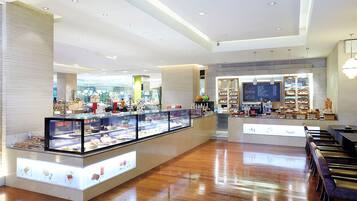 A modern cafe with a central display case of pastries, wooden flooring, and a seating area with tables and chairs.