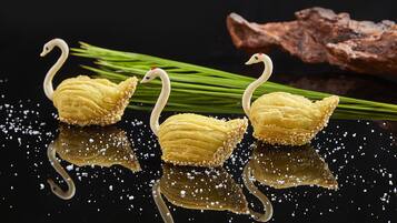 Three swan-shaped pastries on a reflective surface with green onions and a piece of wood in the background.
