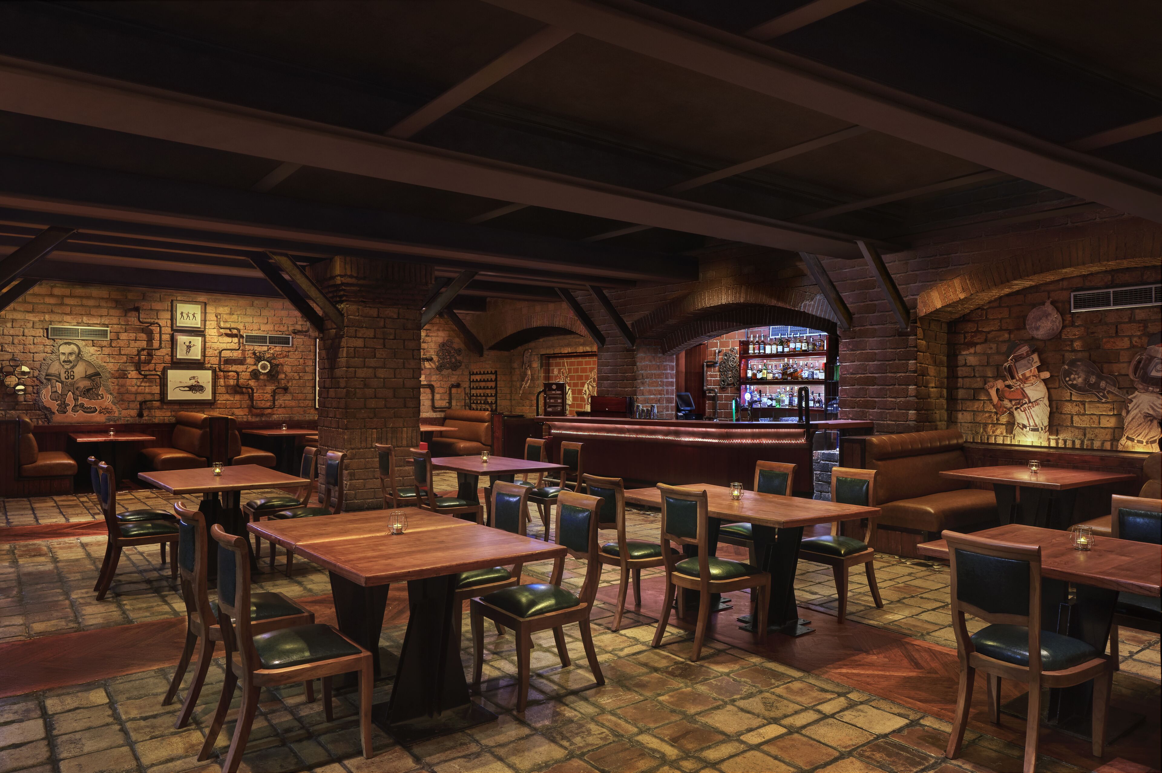 A restaurant with brick walls, wooden tables, and green cushioned chairs.