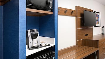 A modern hotel room with a built-in coffee station, a flat-screen TV, and a wooden cabinet.