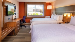 Habitació d'hotel amb dos llits, una taula de treball amb cadira, televisió i finestra amb vista a la ciutat.