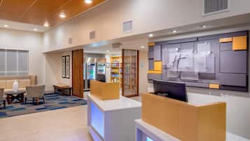 Ein Hotel-Rezeptionsbereich mit Empfangstresen, Sitzgelegenheit und Wanddisplay.