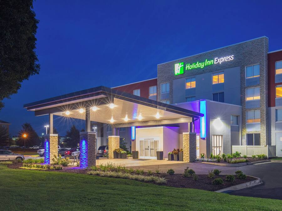 Un hotel Holiday Inn Express amb entrada coberta, il·luminació exterior i una zona enjardinada amb plantes.