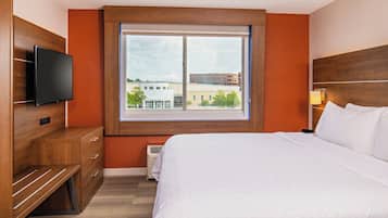 A hotel room with a bed, a TV, a window with a view of buildings, and a heater.
