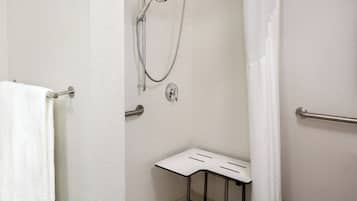 Een kleine badkamer met witte tegels, voorzien van een douche, een handdoekhouder en een handgreep.