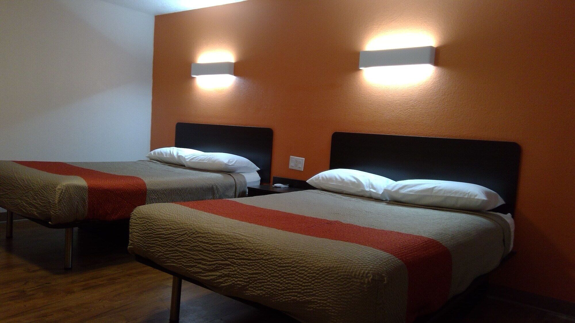Two single beds with headboards, a wall-mounted light fixture, and a wooden floor.