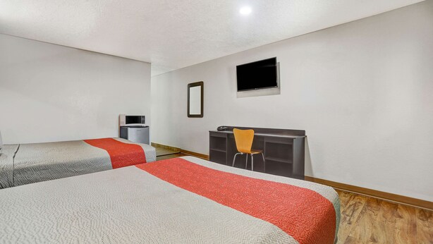 Habitación de hotel con dos camas, un escritorio, una silla, un televisor y un ventanal pequeño.