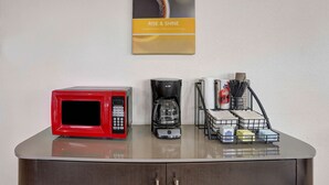 Una encimera de cocina con un microondas rojo, una cafetera negra y una estación para café con azúcar, leche y un portalápices.