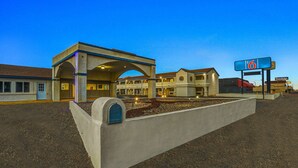 Un motel con un amplio estacionamiento, un área de espera techada y un letrero que indica el número 6.