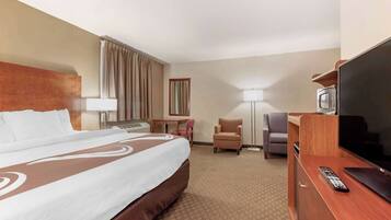 A hotel room with a large bed, a desk with a lamp, a chair, a TV, and a remote control.