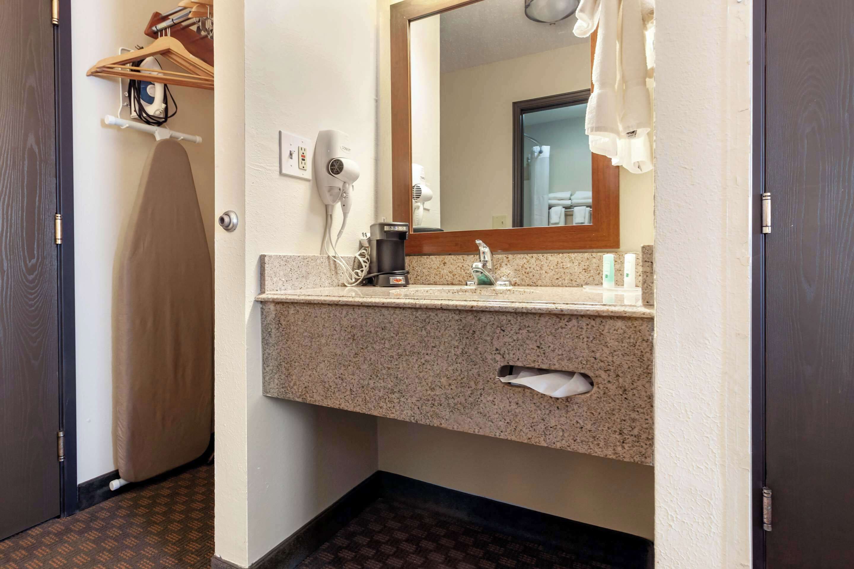 Een hotelbadkamer met een granieten aanrechtblad, een haardroger, een spiegel en een handdoekhouder.