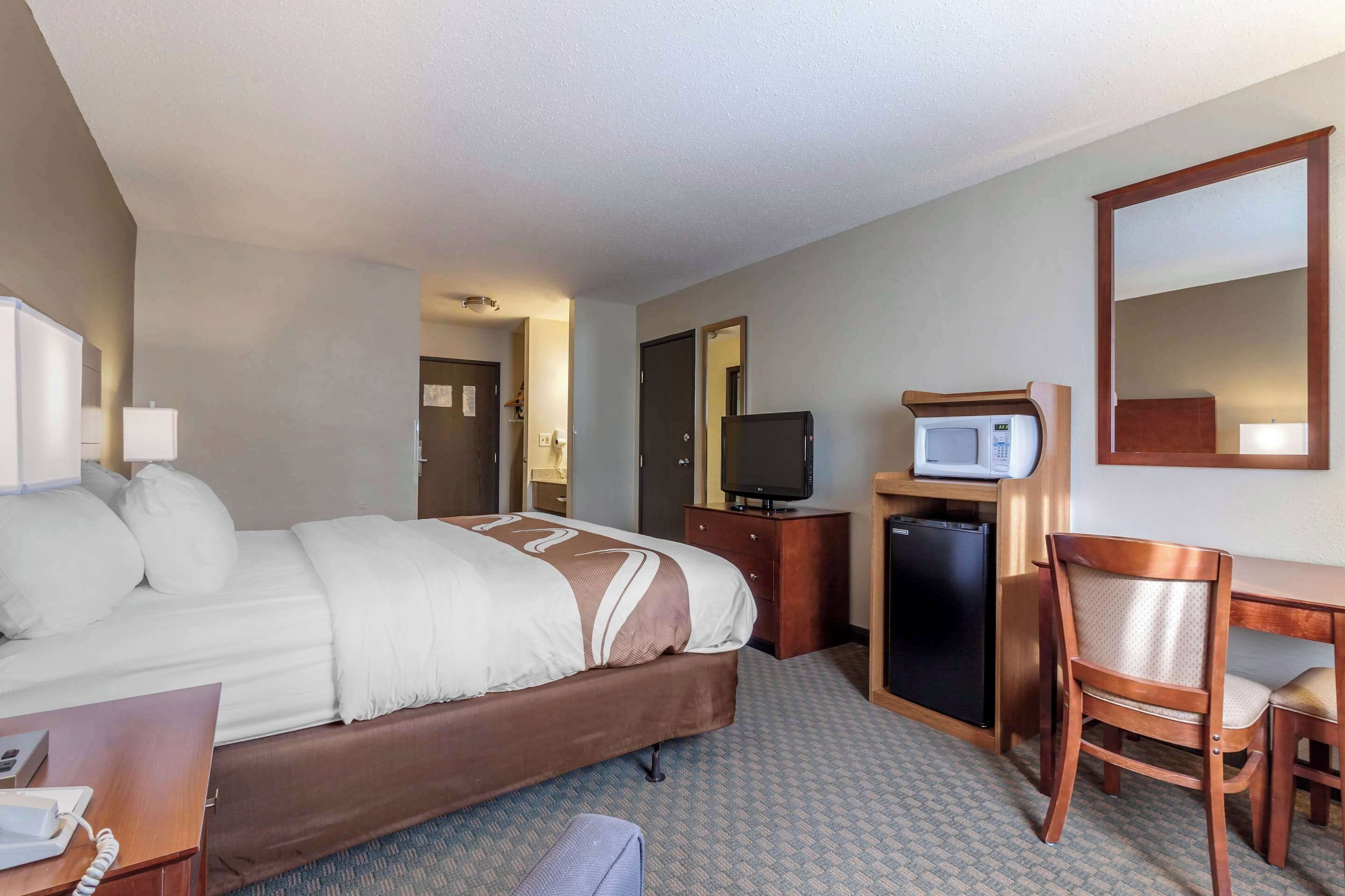 Habitación de hotel con cama, escritorio, silla, microondas y refrigerador.