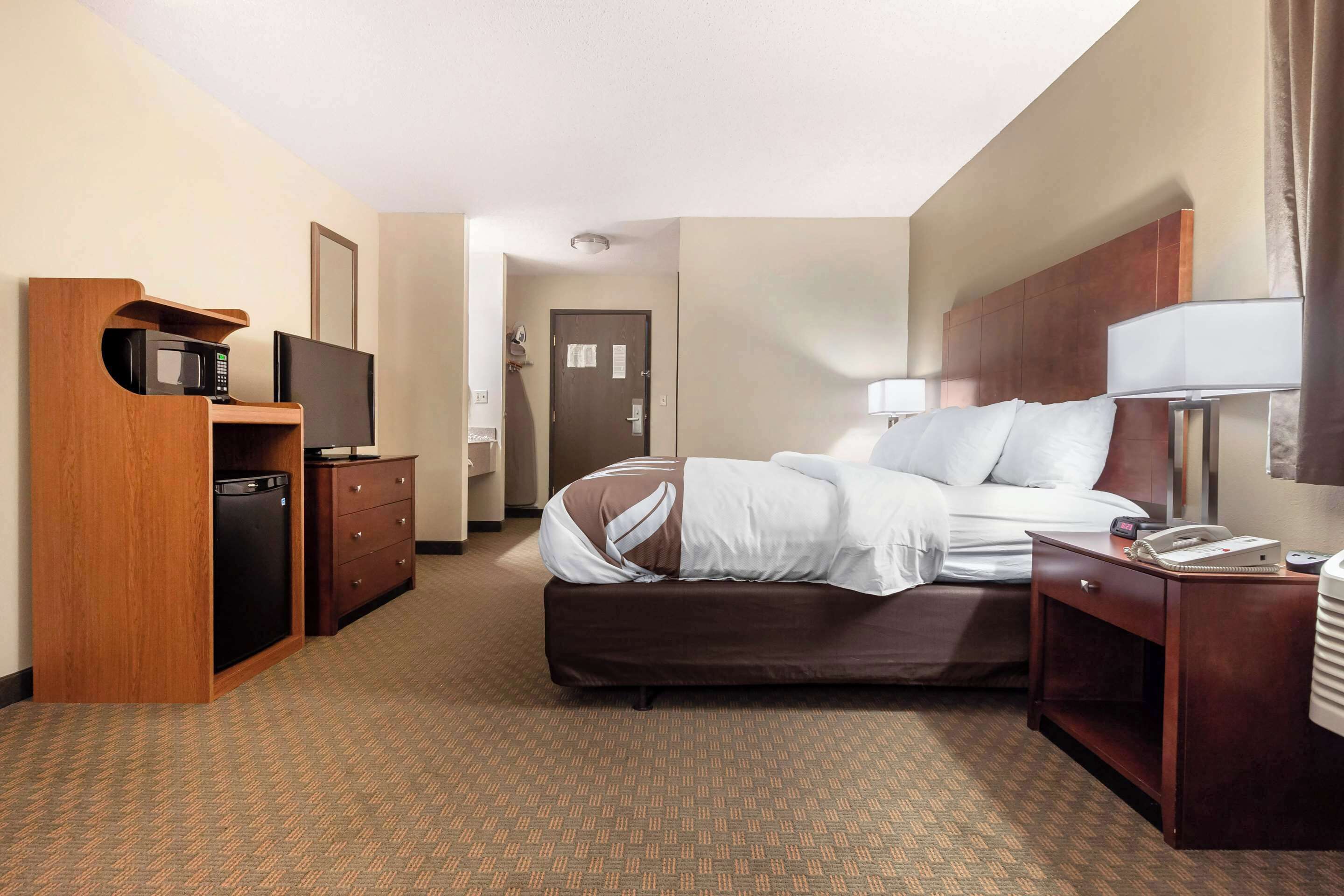 Una habitación de hotel con cama, escritorio con lámpara, televisor y minibar.