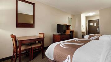A hotel room with a bed, a desk with a chair, a television, and a mirror on the wall.