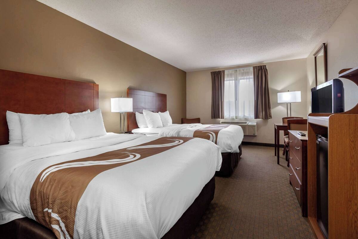 A hotel room with two beds, a desk, a chair, a television, and a window with curtains.
