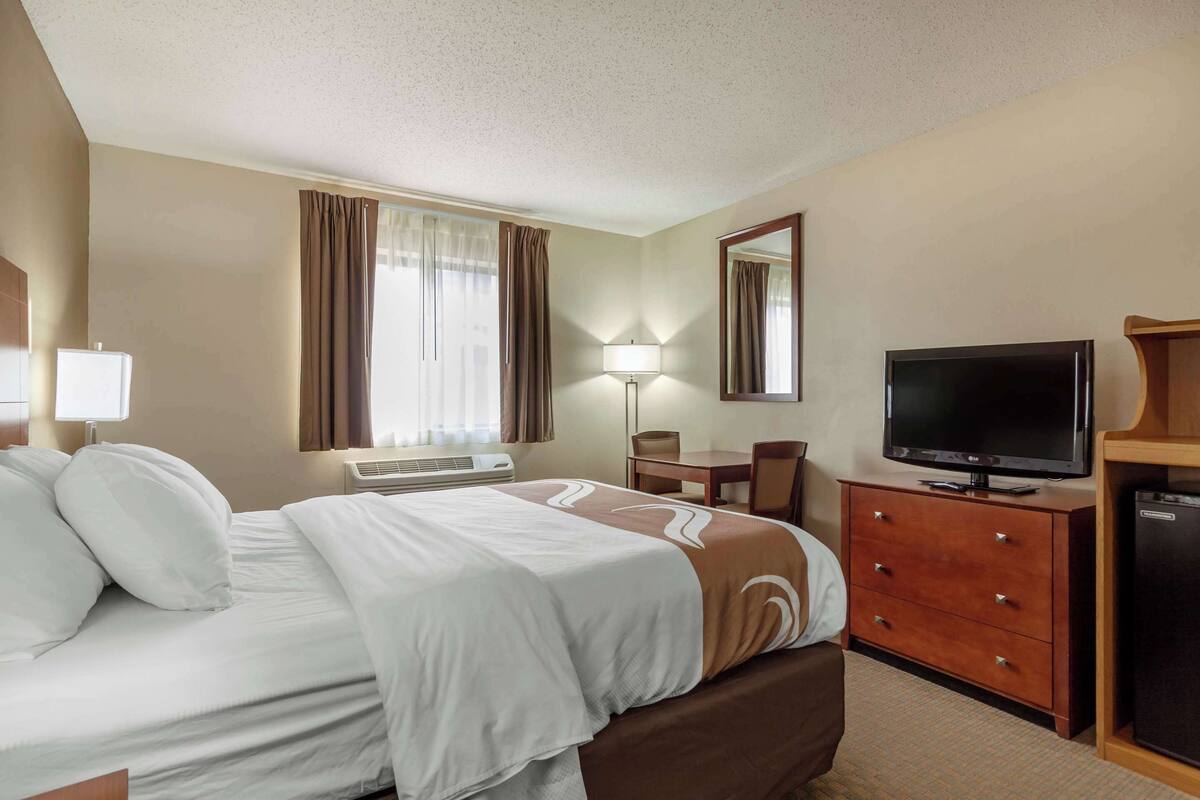A hotel room with a bed, a TV, a desk, and a chair.