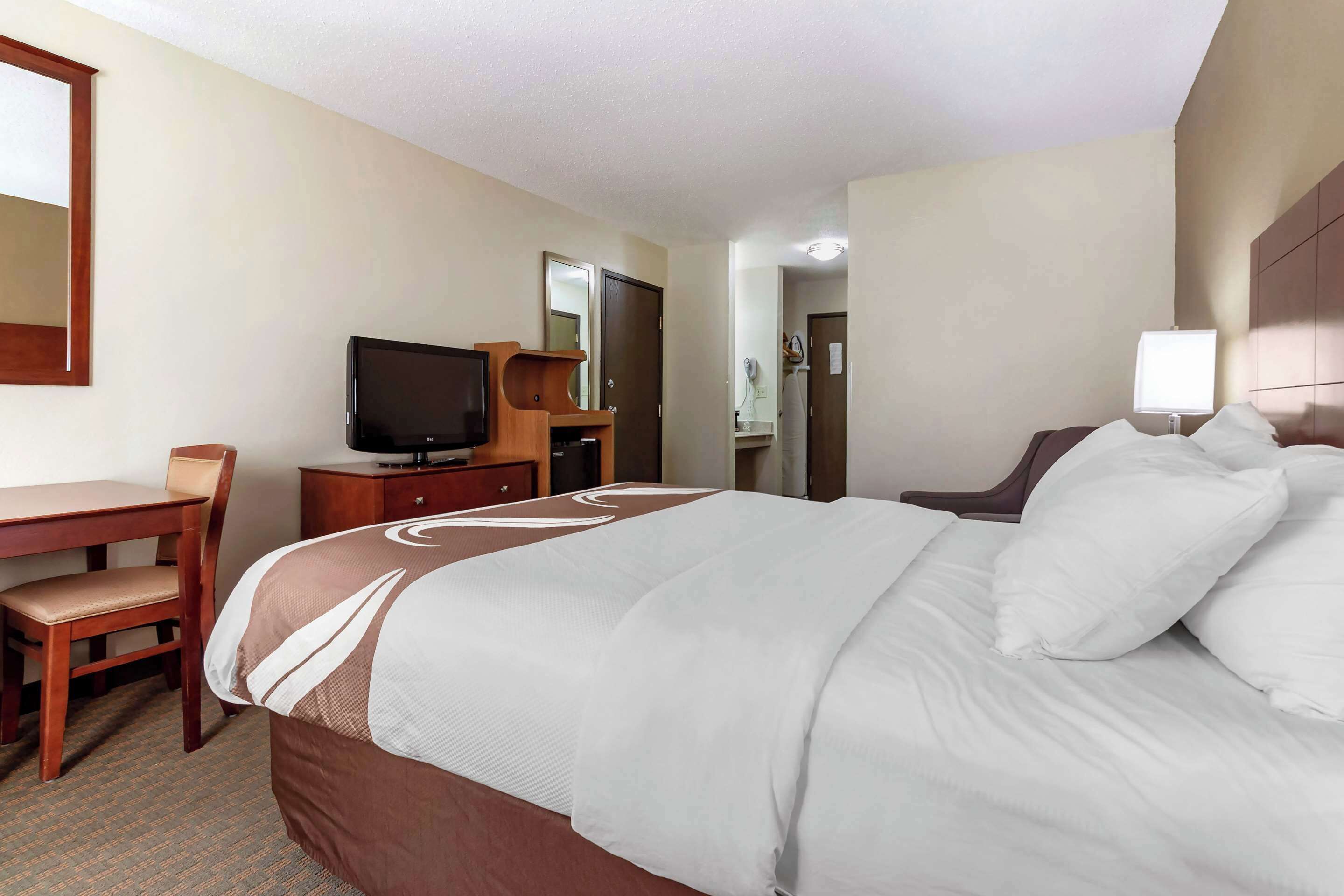 Een hotelkamer met een groot bed, een bureau met stoel, een televisie en een lamp.