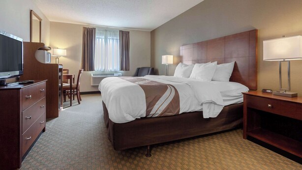 A hotel room with a large bed, a desk with a chair, a television, and a window with curtains. - Quality Inn Hays I-70 (Hays)