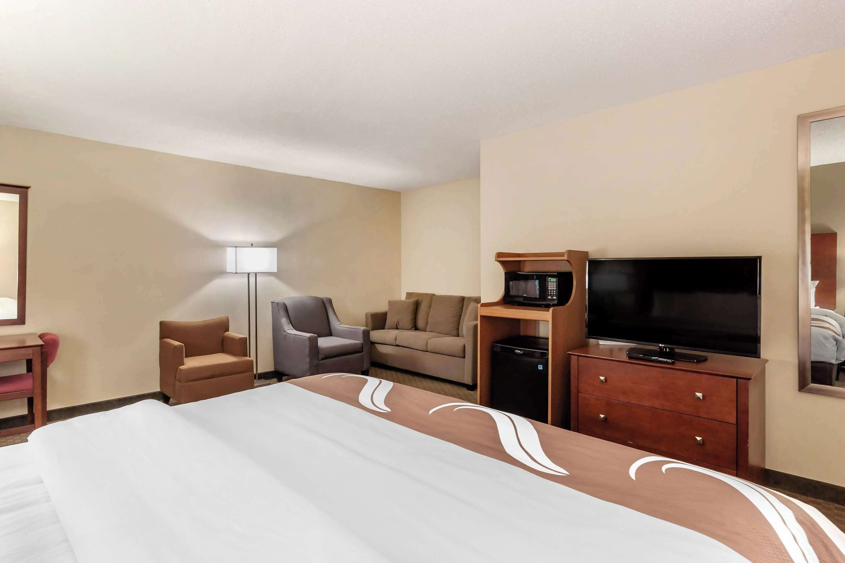 A hotel room with a large bed, a TV, a desk, a chair, and a sofa.