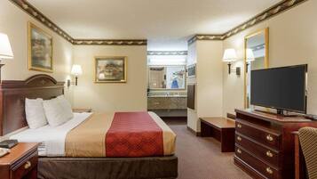 A hotel room with a bed, a dresser, a television, and a bathroom visible through an open door.