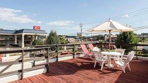 A deck with outdoor seating, a view of a building with a red sign, and a clear sky. - Econo Lodge Grenada (Grenada)