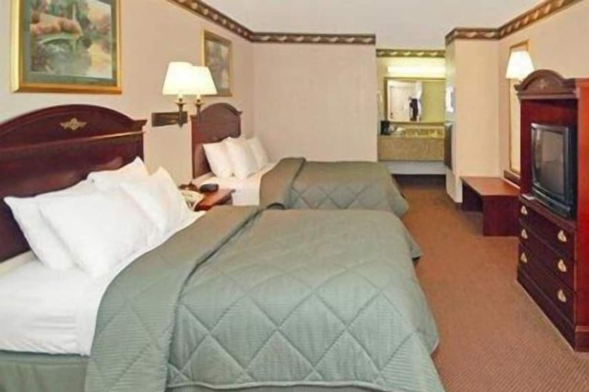 Quarto de hotel com duas camas, uma televisão, um espelho e uma cômoda.