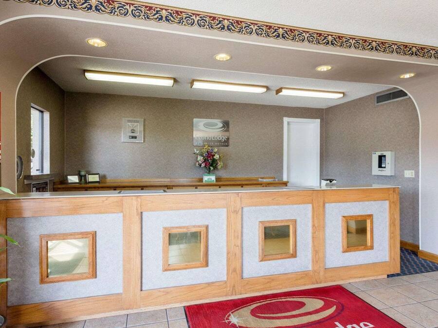 Un mostrador de recepción con alfombra roja, un logo enmarcado y un jarrón de flores.
