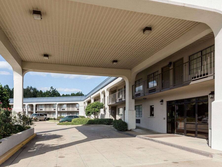 Un hotel con un área exterior cubierta, varios balcones y un estacionamiento.
