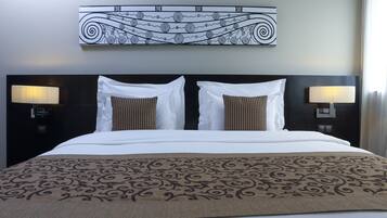 A hotel room with a large bed, two bedside lamps, a decorative wall piece, and a patterned throw blanket.