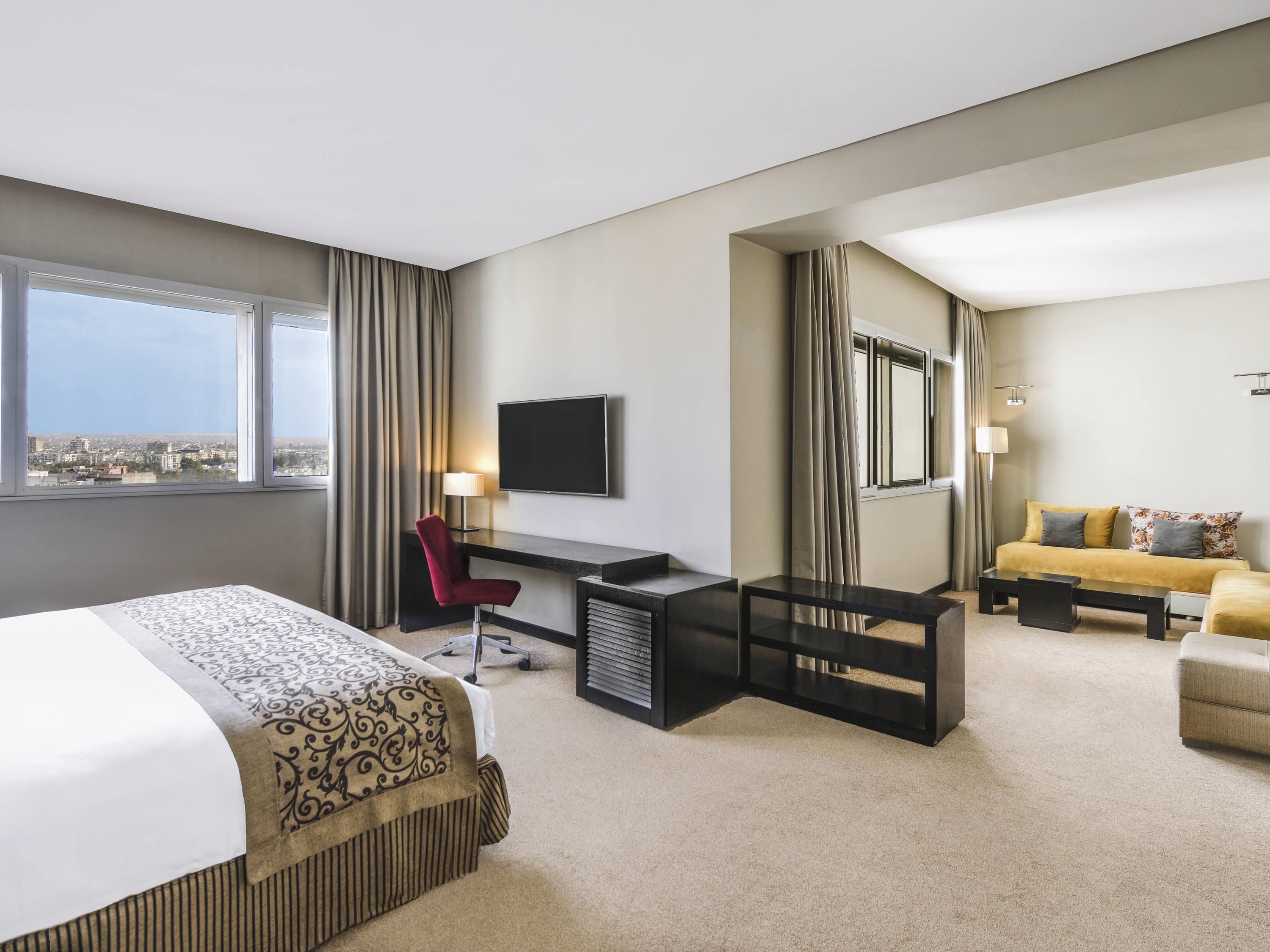 Habitación de hotel con cama, escritorio, sillón, sofá y televisión.