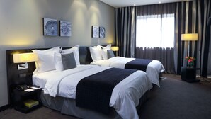 A hotel room with two beds, a nightstand with a lamp, and artwork on the wall.