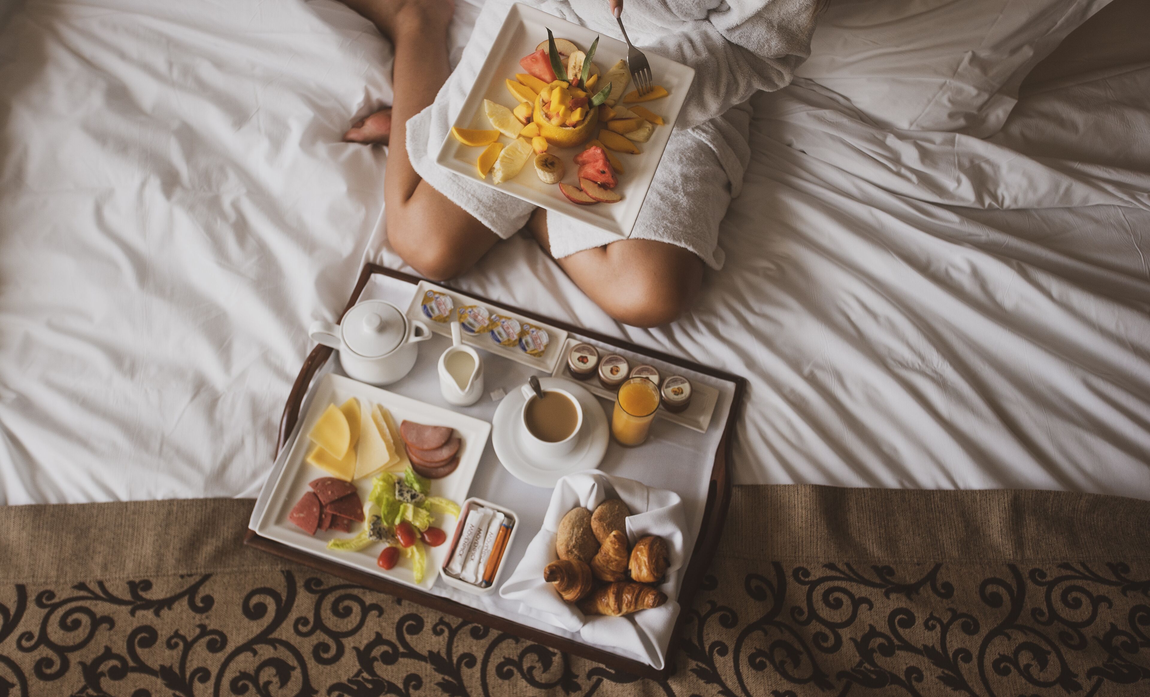 Una bandeja con alimentos para el desayuno, incluyendo frutas, pasteles y salsas, sobre una cama.