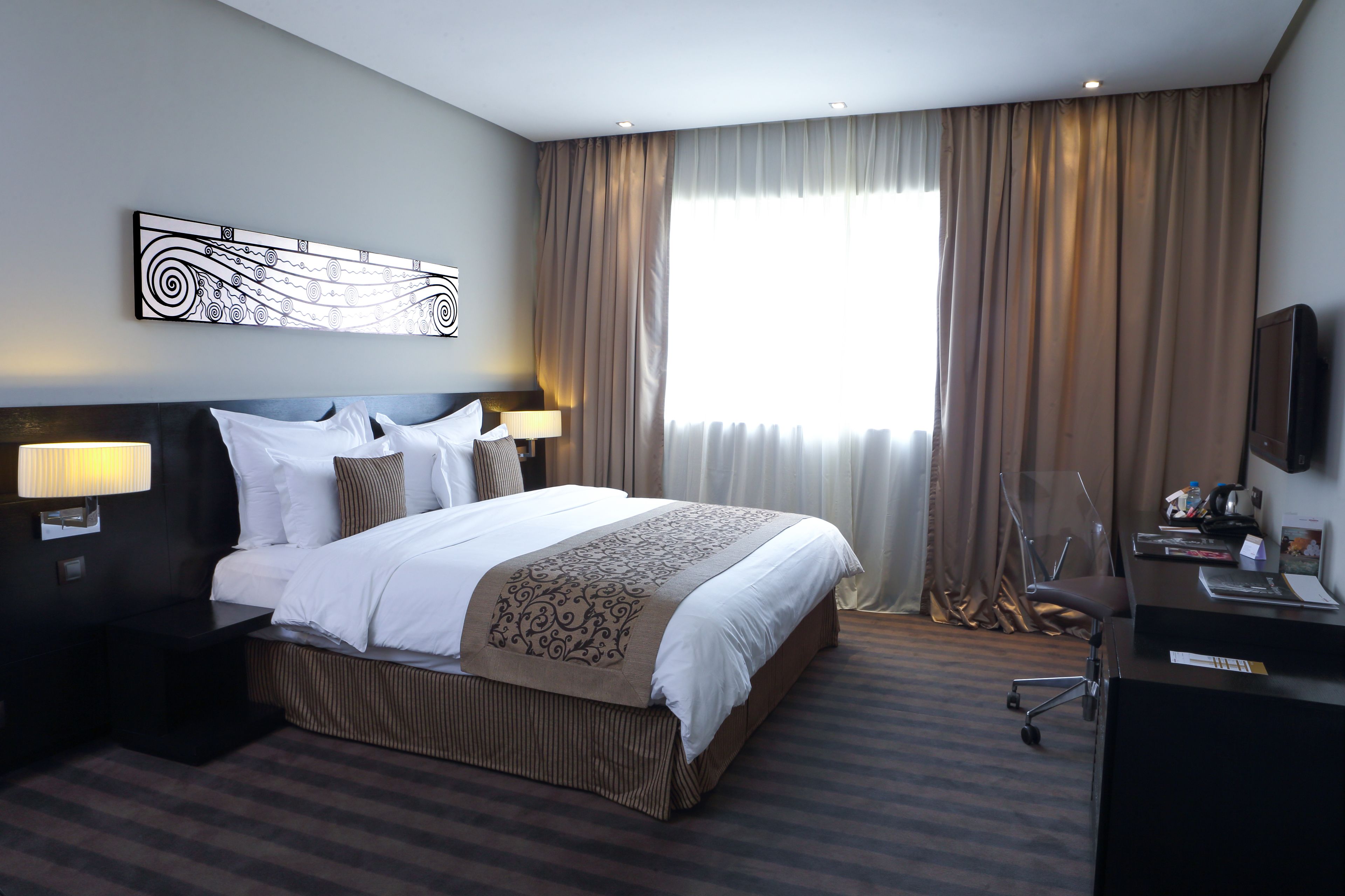A hotel room with a large bed, bedside lamps, a flat-screen TV, and a desk with a laptop.