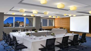 Une salle de conférence équipée d’une longue table, de chaises, d’un écran de projection et de grandes fenêtres donnant sur la ville.