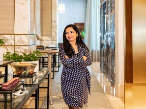 A woman in a patterned dress standing in a hotel corridor with marble walls, a glass table with pastries, and a plant. - Mövenpick Hotel Casablanca (Casablanca)