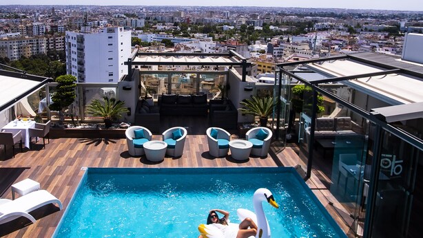 A rooftop pool with a swan float, lounge chairs, and a city view.