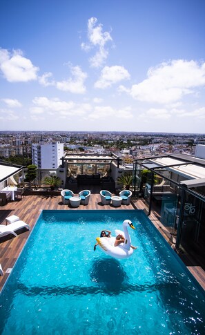 Una piscina en la azotea con un flotador de cisne, sillas de descanso y vistas a la ciudad.