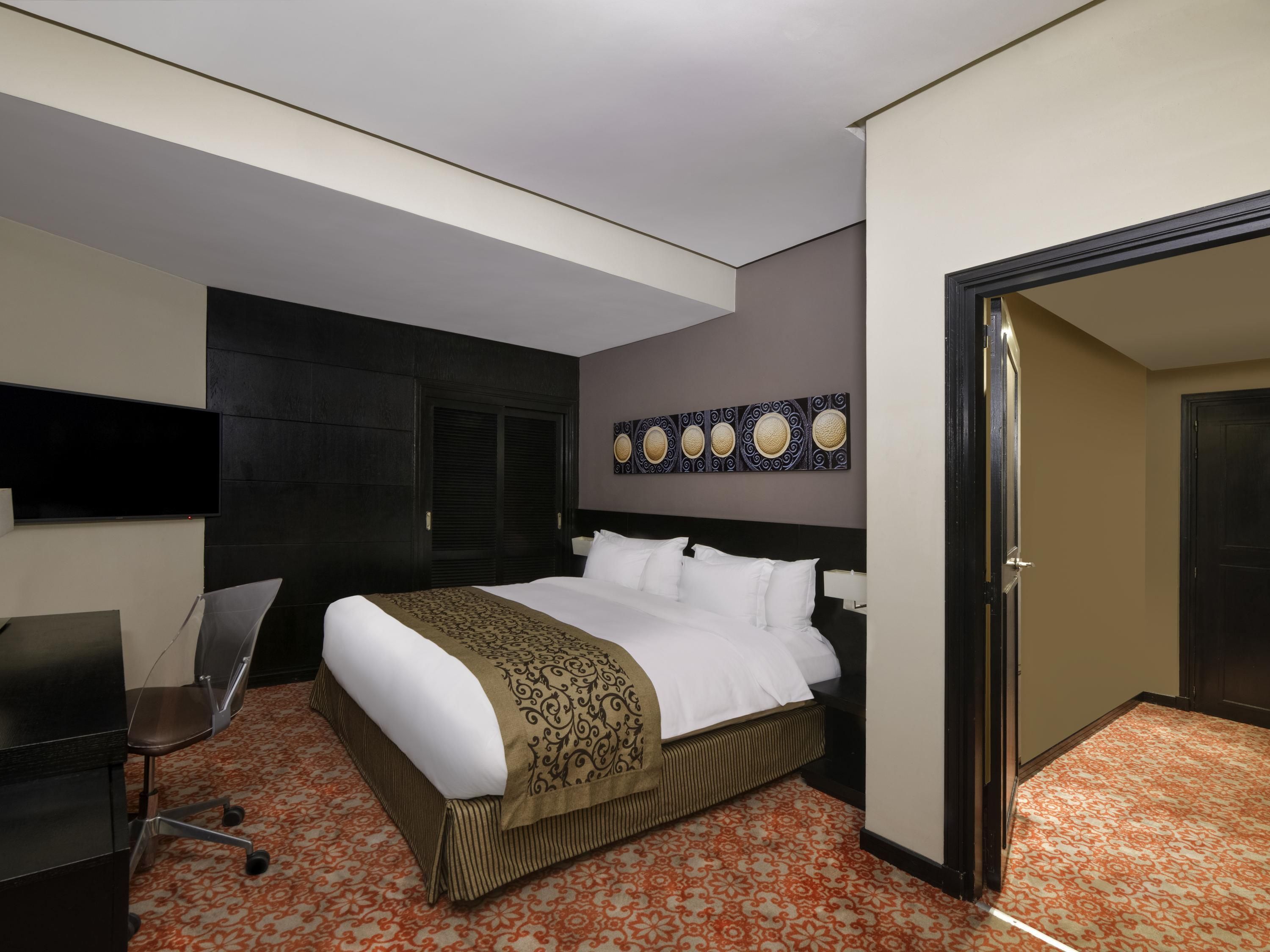 Una habitación de hotel con cama, escritorio, silla, televisor y puerta.